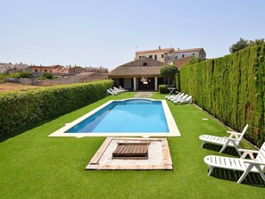 A rectangular swimming pool with a wooden deck in the center, surrounded by white lounge chairs. - Holiday Home in Llubi With Swimming Pool (Llubi)