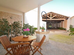 An outdoor patio with a wooden table and chairs, surrounded by potted plants and a stone wall. - Holiday Home in Llubi With Swimming Pool (Llubi)