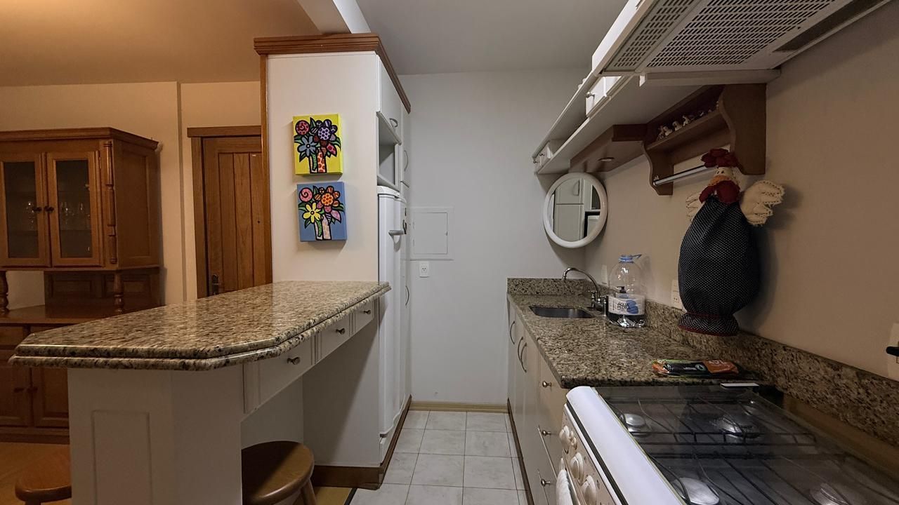 A compact kitchen with a granite countertop, a built-in oven, and a microwave. There are wooden cabinets and a small stool.