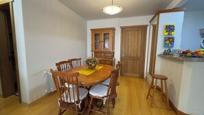 Un coin repas avec une table et des chaises en bois, un buffet avec des portes en verre et un comptoir de cuisine agrémenté de fruits.