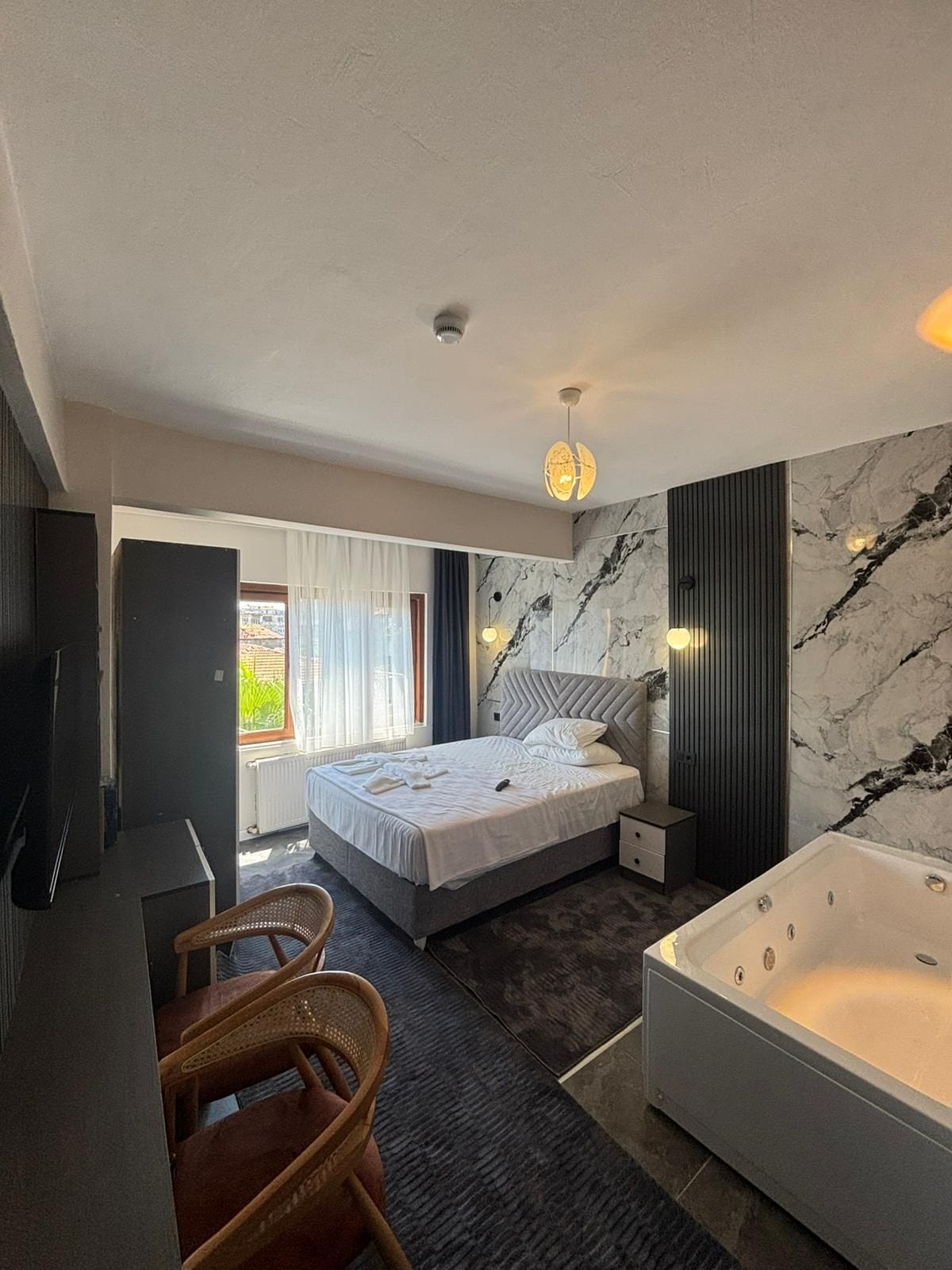 Une chambre à coucher moderne comprenant un lit, un coin salon avec un fauteuil, une grande baignoire et un téléviseur.