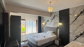 A modern bedroom with a bed, a sitting area with a chair, a large bathtub, and a television.