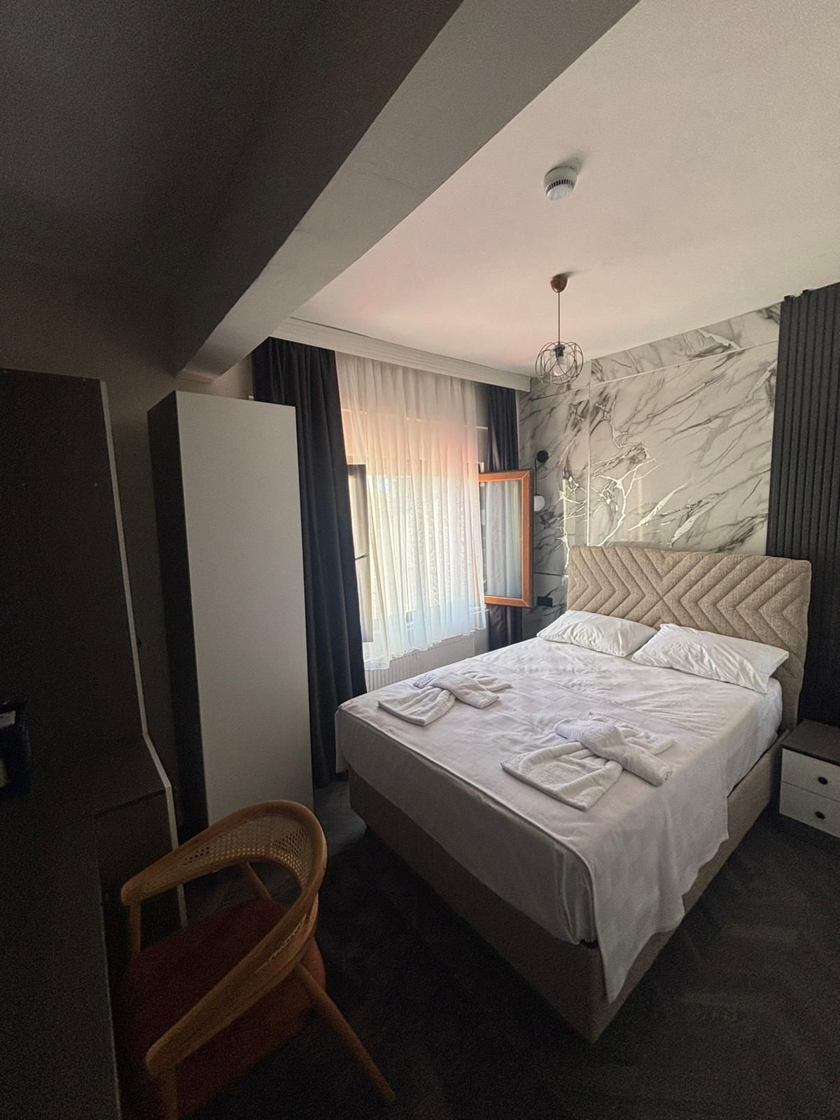 A hotel room with a bed, a chair, a nightstand, and a wall with a marble-like design.