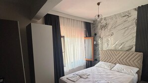 A hotel room with a bed, a chair, a nightstand, and a wall with a marble-like design. - Klas Otel (Karasu)
