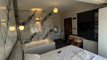 A modern hotel room with a large bed, a separate bathroom with a bathtub, a desk, and a chair.