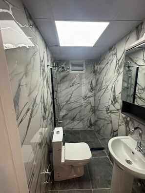 A bathroom with a toilet, sink, and shower area, featuring marble walls and a skylight. - Klas Otel (Karasu)
