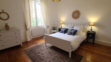 Ein Schlafzimmer mit einem Bett, Nachttischen, einer Kommode, einem Fenster mit Vorhängen und einem Teppich.