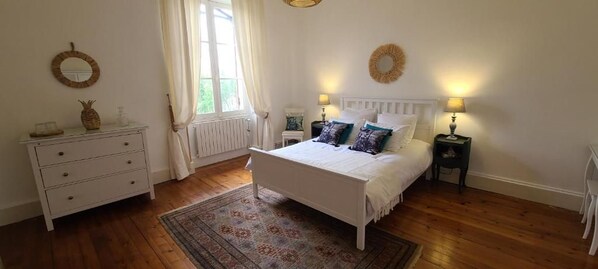 A bedroom with a bed, bedside tables, a dresser, a window with curtains, and a rug.