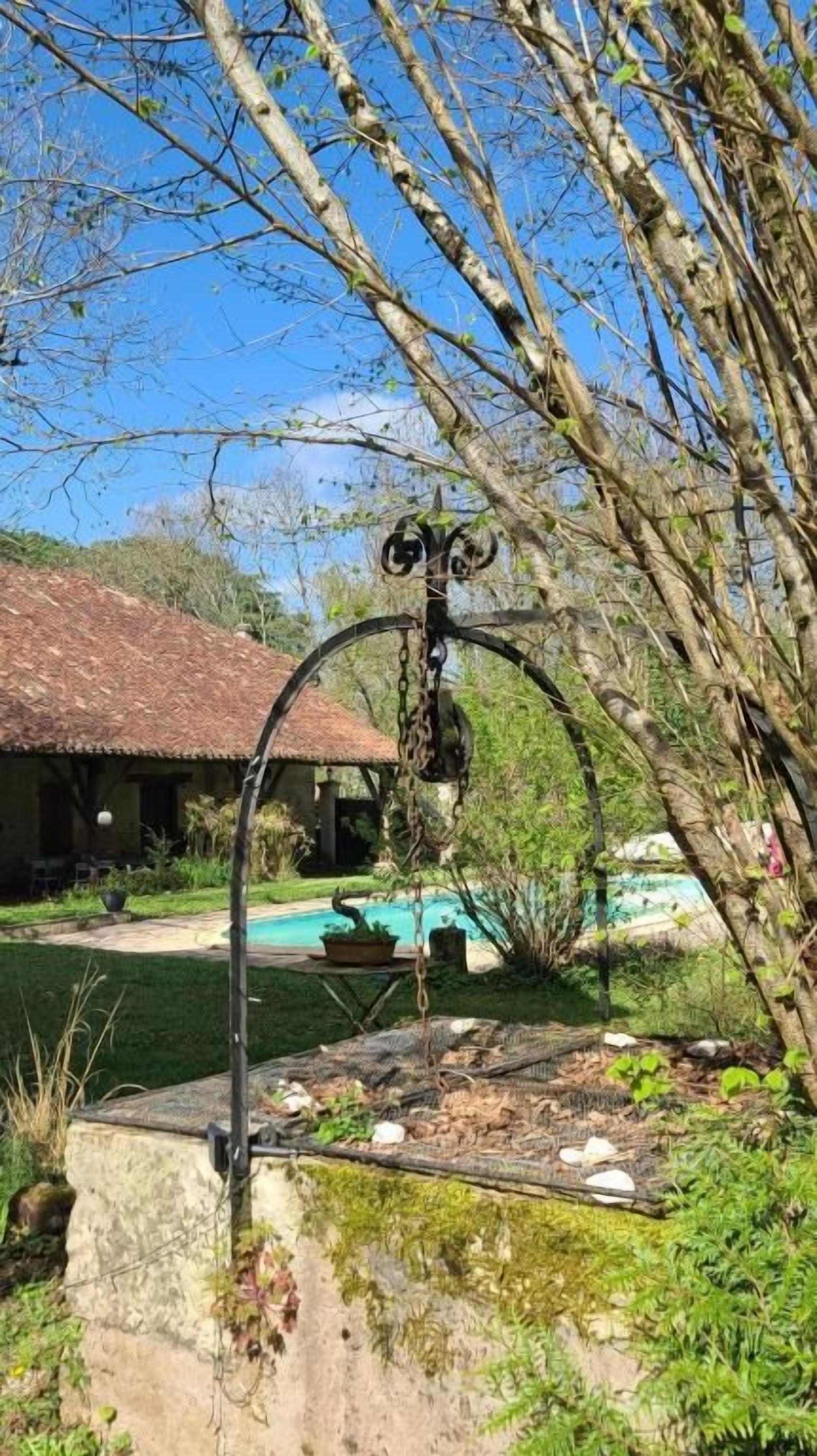 Un jardín con una estructura metálica, una piscina y un edificio con tejado rojo.