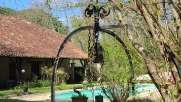 Un jardín con una estructura metálica, una piscina y un edificio con tejado rojo.