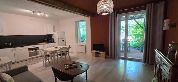 Una cocina moderna con armarios blancos, un comedor con mesa y sillas, y un amplio ventanal corredero que da a un espacio exterior.