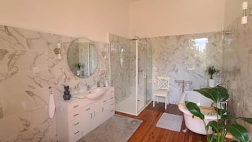 Une salle de bain aux murs recouverts de marbre, avec une douche en verre, un lavabo blanc et une plante en pot.