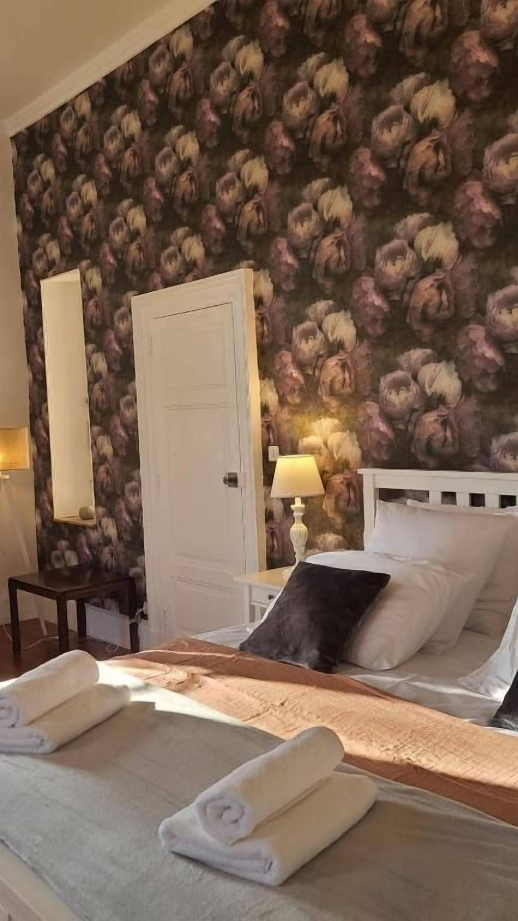 A hotel room with a bed, a bedside table, a lamp, and a door.