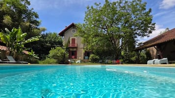 Ein Swimmingpool mit klarem, blauem Wasser, umgeben von Liegestühlen und einem Gebäude mit rotem Dach.