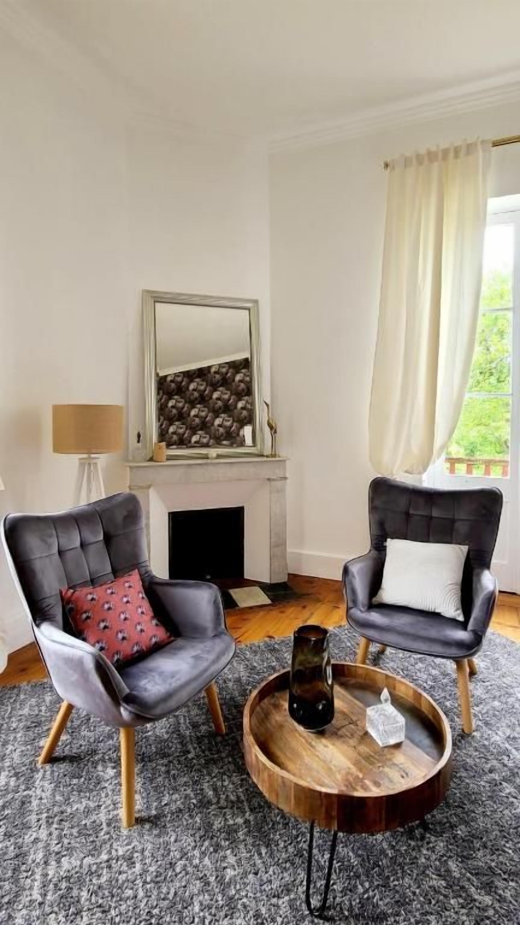 A room with two leather armchairs, a round wooden coffee table, a fireplace, and a large mirror above it.