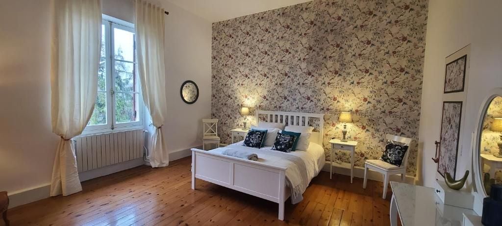 A bedroom with a white bed, floral wallpaper, and two bedside tables with lamps.