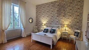 A bedroom with a white bed, floral wallpaper, and two bedside tables with lamps.