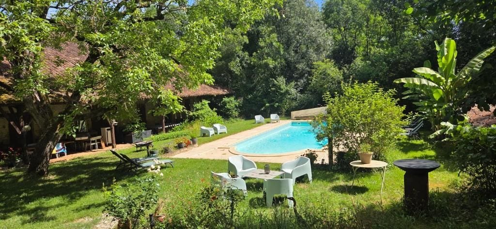 Un patio trasero con piscina, rodeado de vegetación y mobiliario exterior.