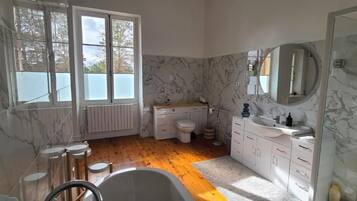 Une salle de bain avec une baignoire, des toilettes, un lavabo et une grande fenêtre.