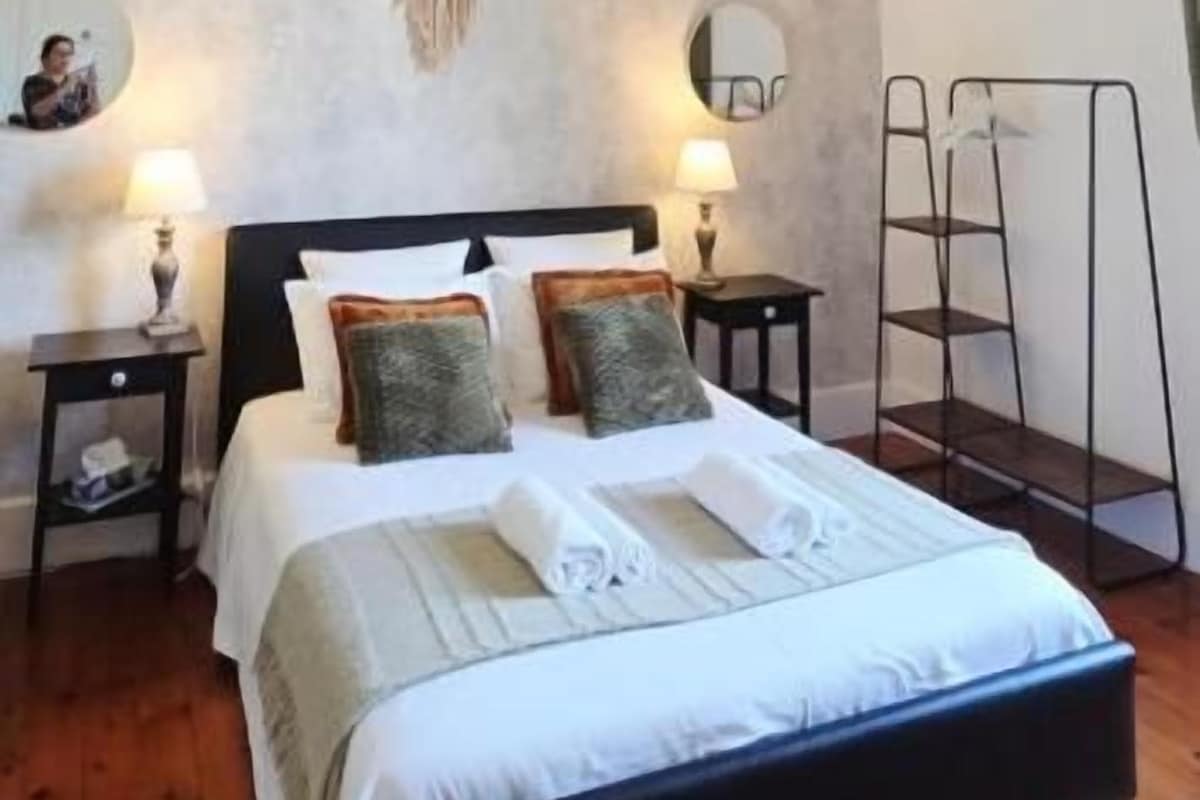 Un dormitorio con cama, lámparas de noche, una lámpara colgante y una escalera adosada a la pared.