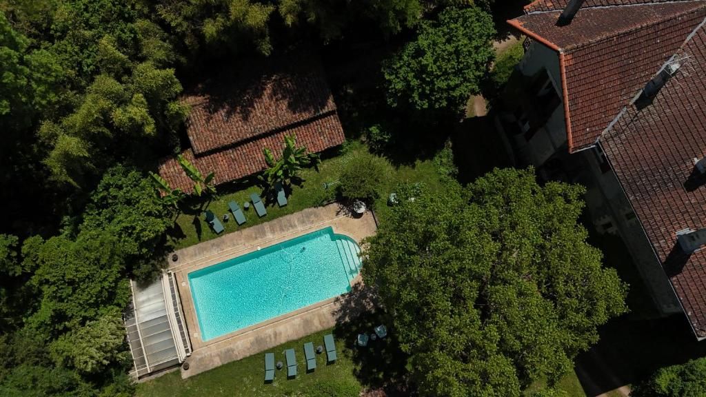 An aerial view of a property with a swimming pool surrounded by trees, a covered patio area, and a building with a red-tiled roof.
