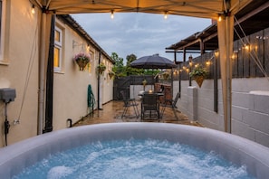 An outdoor hot tub area with a table and chairs, surrounded by a covered patio with string lights. - Cosy Private House with Hot Tub (Leeds)