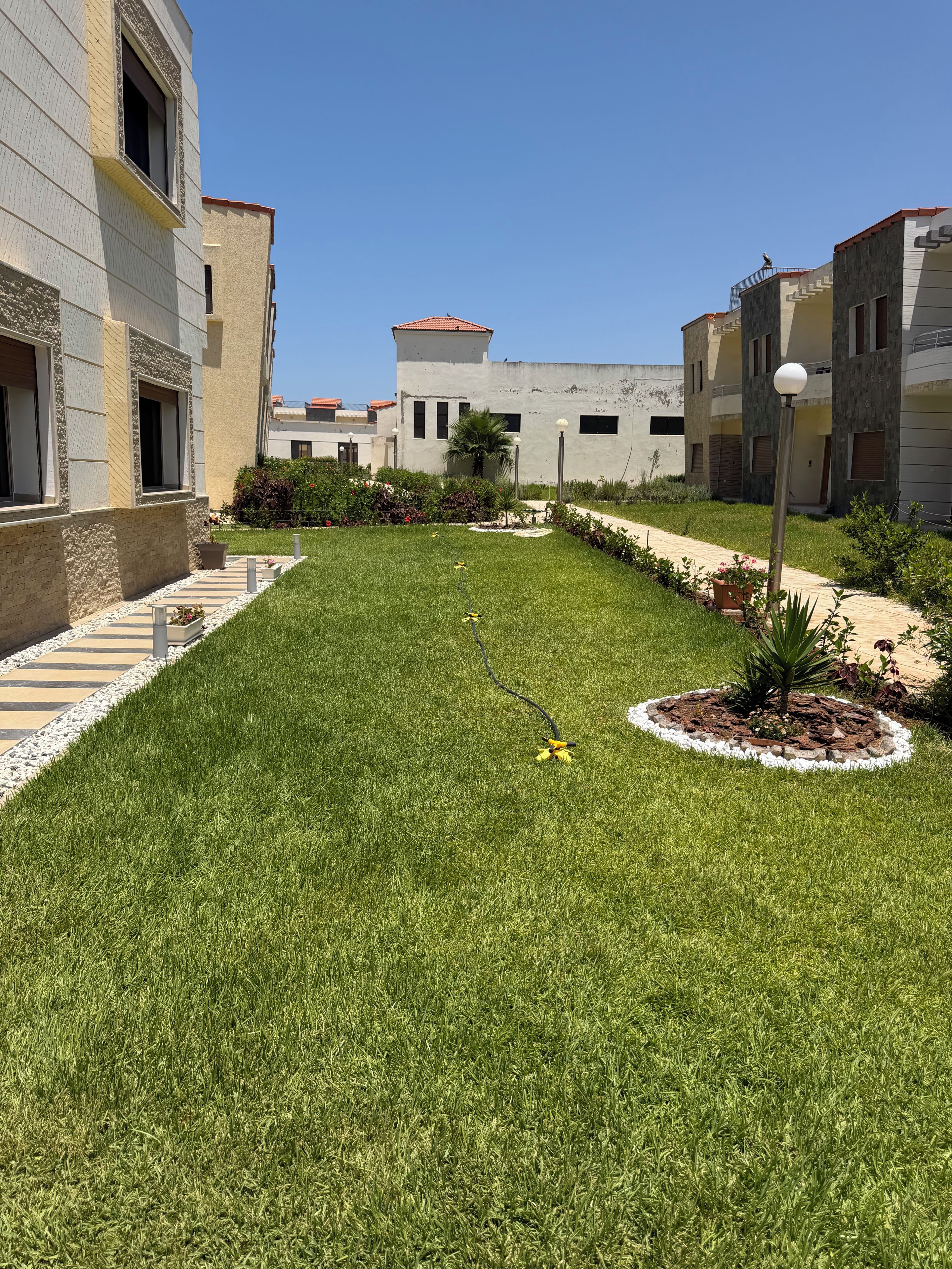 A well-maintained grassy courtyard with a pathway, surrounded by buildings with balconies and windows.
