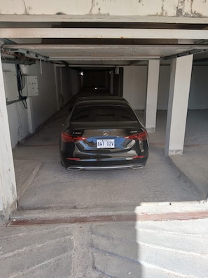 A black car parked in a parking garage with concrete pillars and a visible electrical box on the wall.