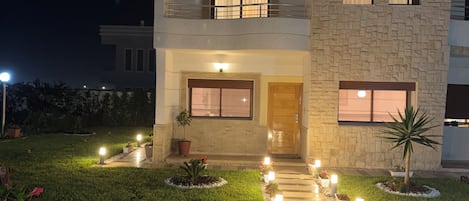 A two-story house with a stone facade, a balcony, and a well-lit entrance.