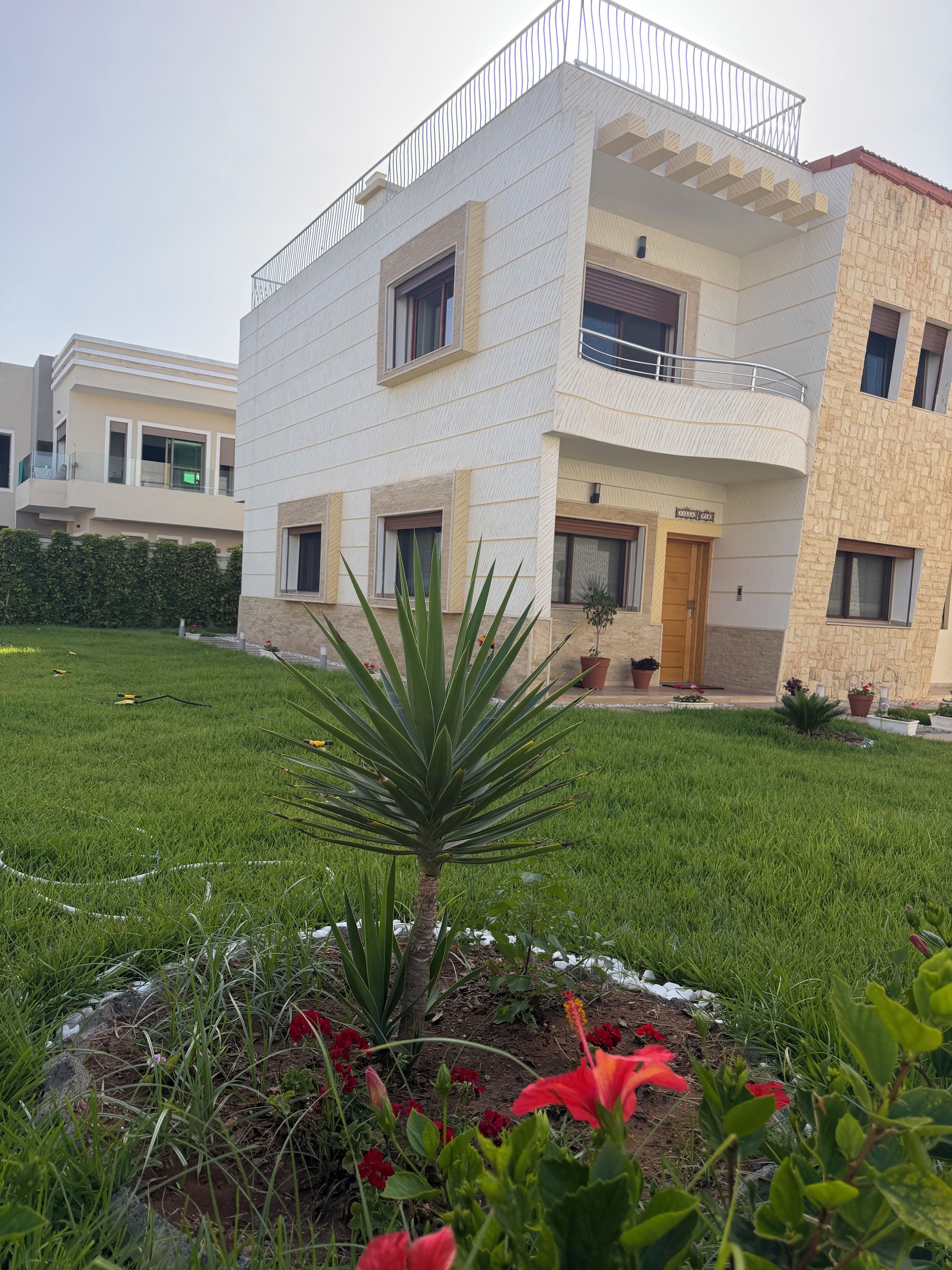 A modern two-story building with balconies, a well-maintained lawn, and potted plants.