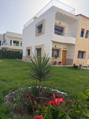A modern two-story building with balconies, a well-maintained lawn, and potted plants.