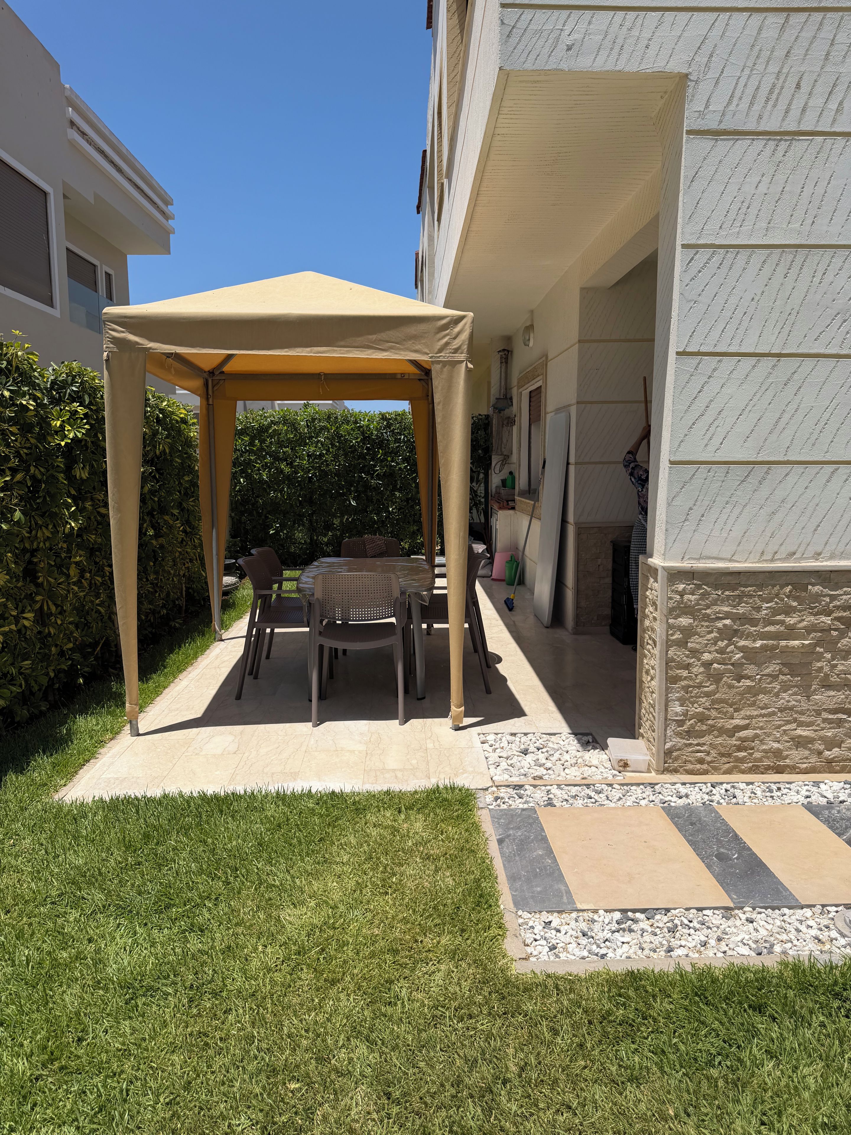 Un espace extérieur abrité, avec une table et des chaises, situé à côté d’un bâtiment dont la façade est en pierre.