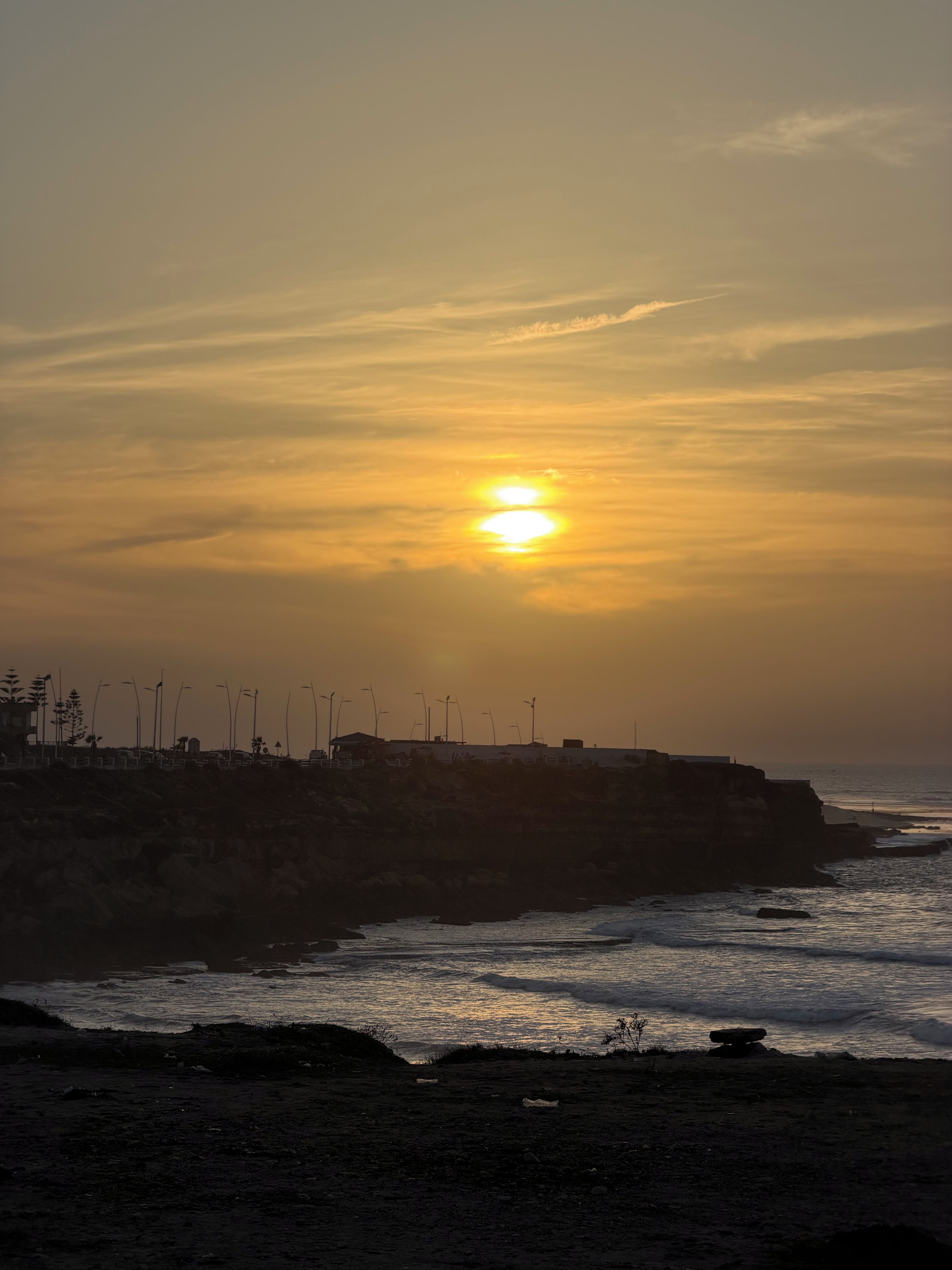 A sunset over a coastal landscape with wind turbines and a rocky shoreline.