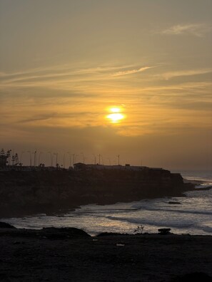 A sunset over a coastal landscape with wind turbines and a rocky shoreline.
