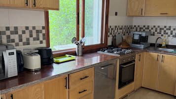 Une cuisine avec des meubles en bois, un lave-vaisselle en acier inoxydable, une cuisinière à gaz et une fenêtre donnant sur un paysage verdoyant.