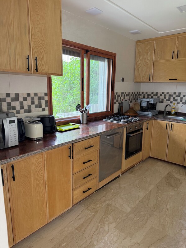 A kitchen with wooden cabinets, a stainless steel dishwasher, a gas stove, and a window with a view of greenery.