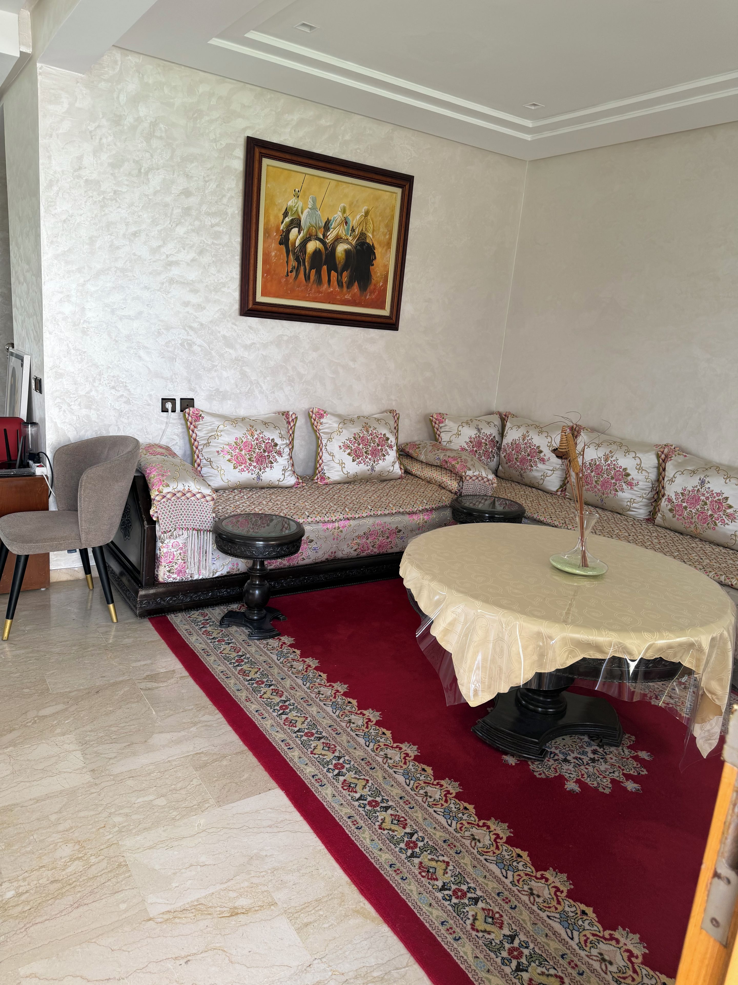 A living room with a sofa set, a round table, a patterned rug, and a painting on the wall.
