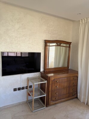 A room with a wooden dresser, a television mounted on the wall, and a small shelf unit.