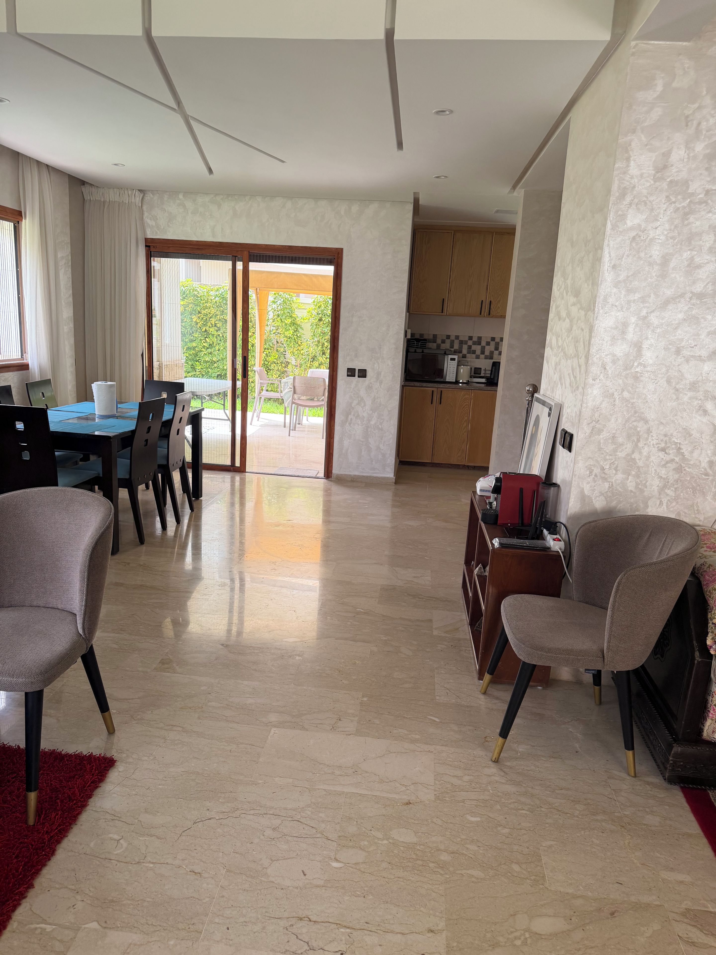 A spacious living area with a dining table, chairs, a kitchen, and a sliding glass door leading to a patio.