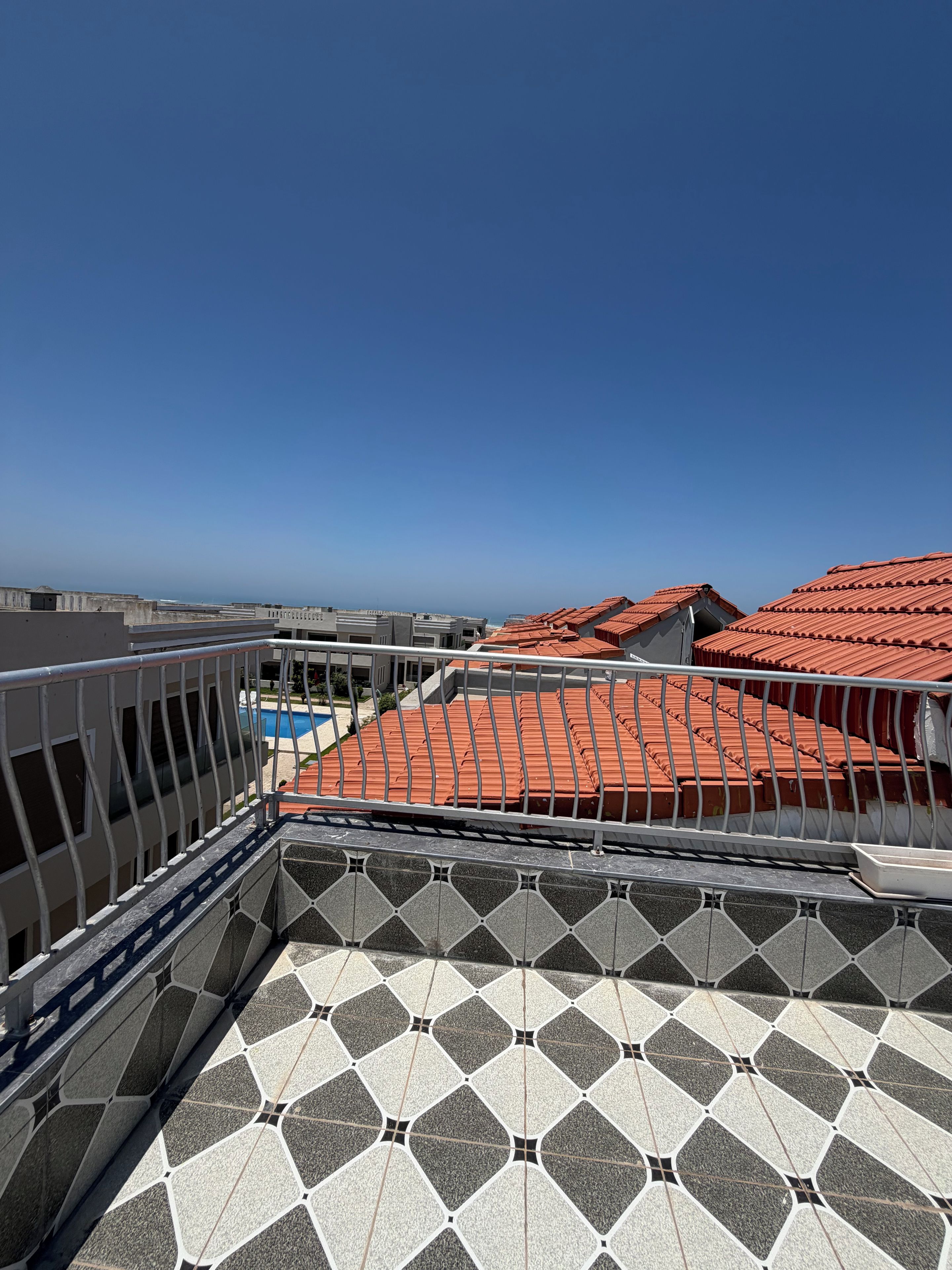 Une terrasse sur le toit avec un sol à motifs, une piscine et des toits recouverts de tuiles rouges.