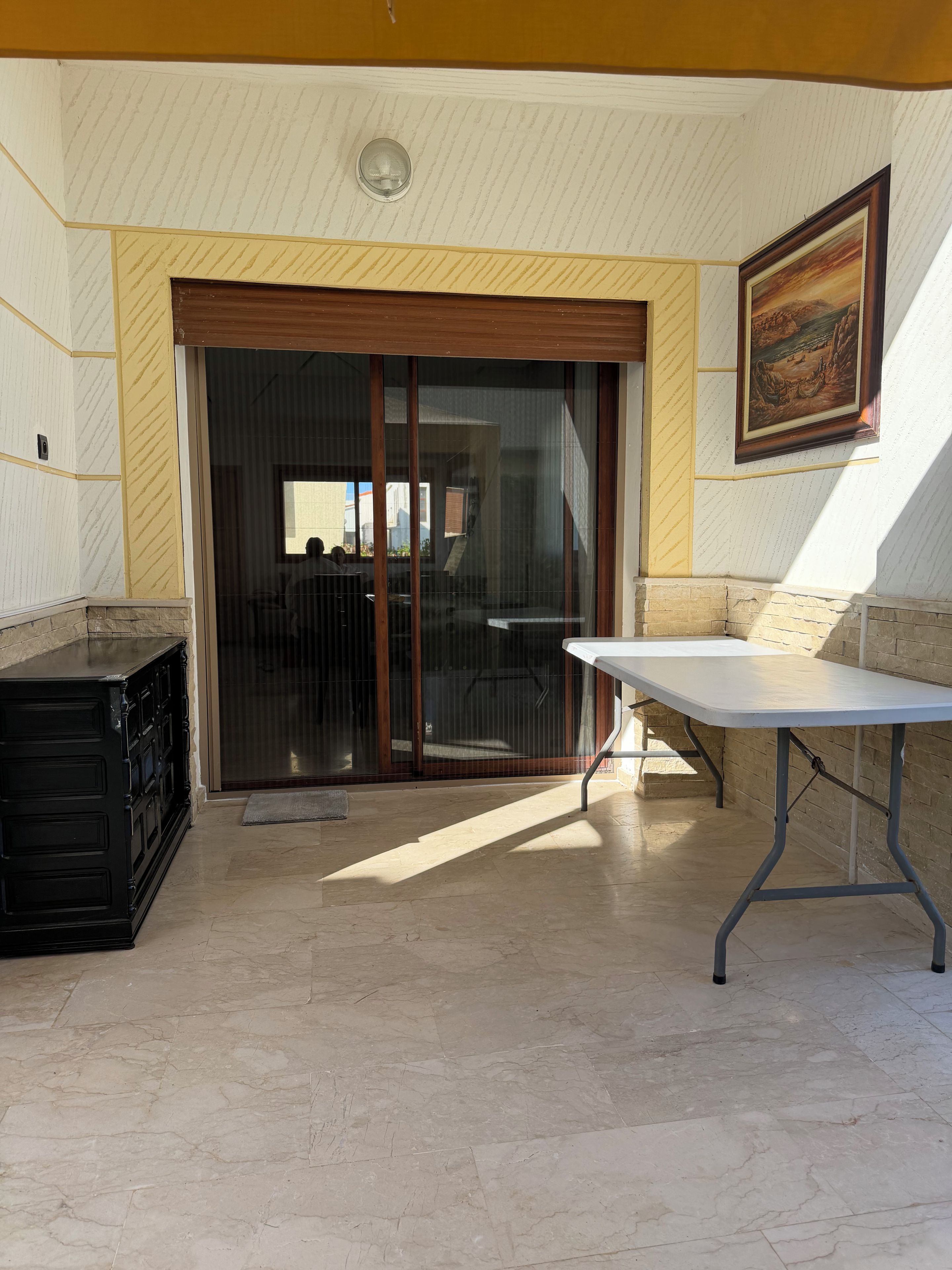 Une pièce dotée d’une porte-fenêtre coulissante, d’une table blanche et d’un meuble noir.