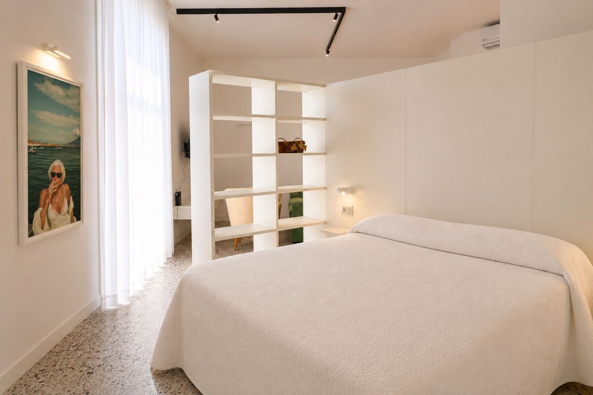 Un dormitorio con cama, pared blanca, un cuadro y estantería empotrada.