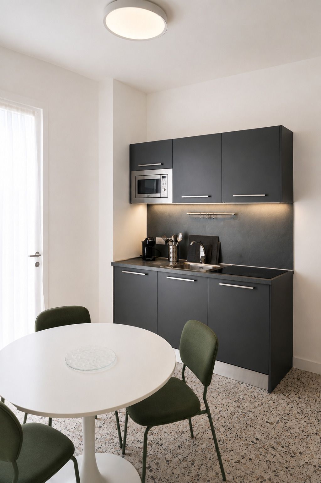 Una cocina moderna con armarios oscuros, microondas, cafetera y una mesa de comedor redonda con sillas.