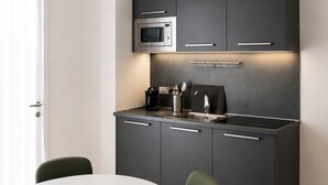 Uma cozinha moderna com armários escuros, micro-ondas, máquina de café e uma mesa de jantar redonda com cadeiras.