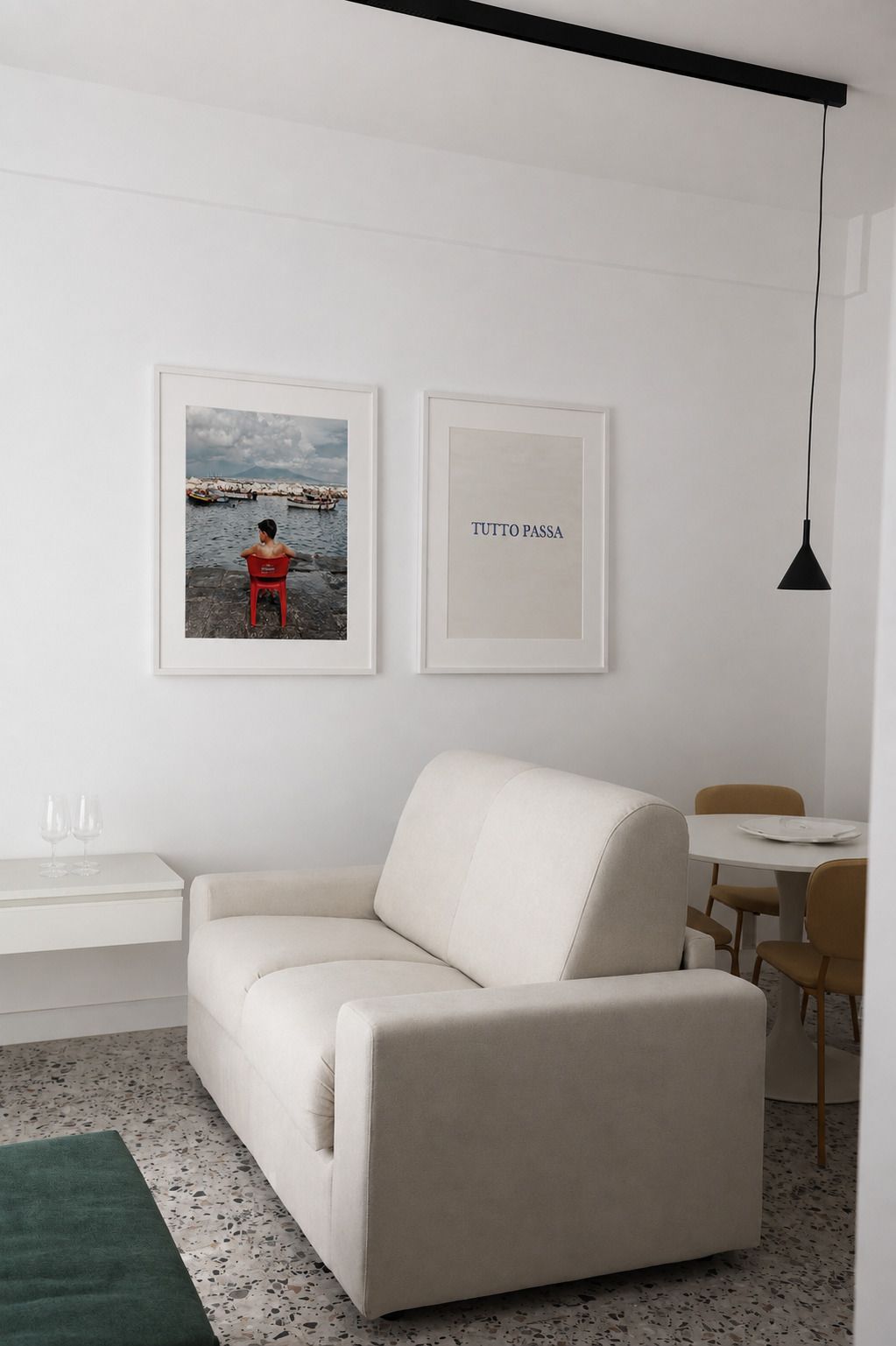 Una sala de estar minimalista con un sofá, una mesa de comedor y dos cuadros en la pared.