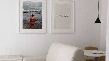 Una sala de estar minimalista con un sofá, una mesa de comedor y dos cuadros en la pared.