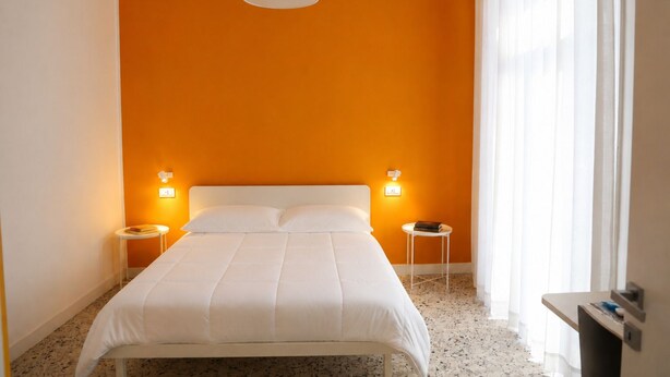 Quarto de hotel com cama, duas mesas de cabeceira, cabeceira branca e luminária pendente.