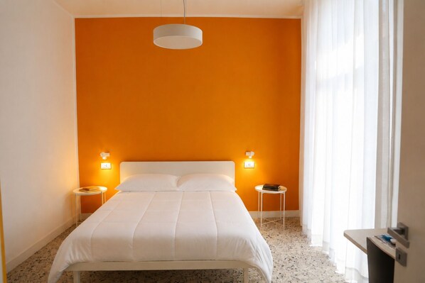 Una habitación de hotel con una cama, dos mesitas de noche, un cabecero blanco y una lámpara colgante.