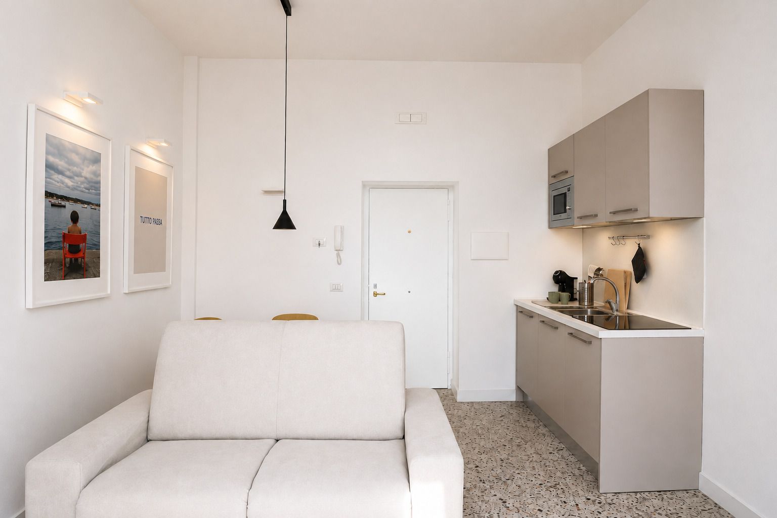 Un espacio habitable compacto con sofá, kitchenette y una puerta que da a otra habitación.