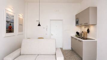 Un espacio habitable compacto con sofá, kitchenette y una puerta que da a otra habitación.